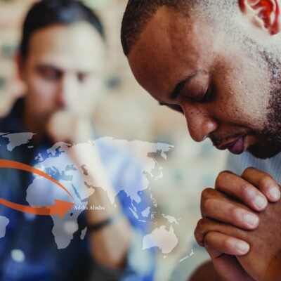 Two men praying over diverse discipleship with a faded world map overlayed on the screen.