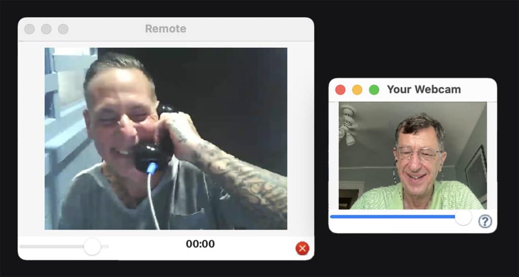 Two men on a web call, one holding a phone in prison.