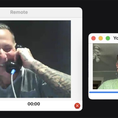 Two men on a web call, one holding a phone in prison.