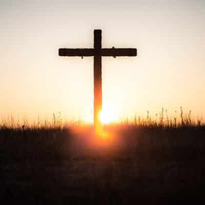 Silhouette of a cross on a hilltop with a orange and yellow sunset in the background