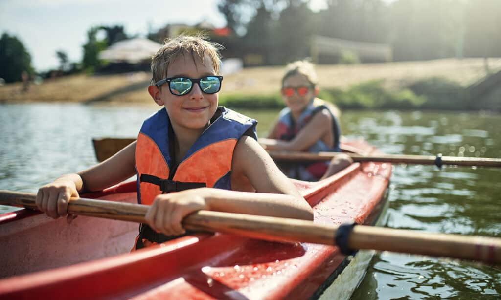 Two boys kayaking in an orange kayak on a lake.