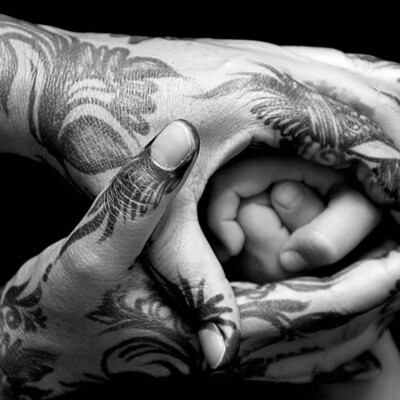 Two sets of hands that are wrapped around each other in prayer. One set of hands has Indian style henna designs.
