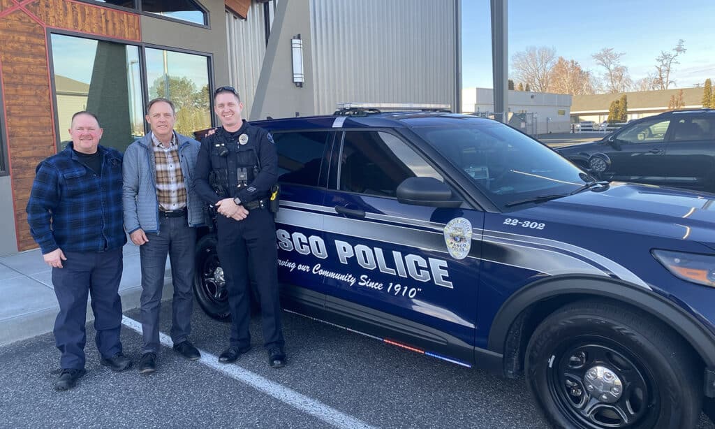 A group of Navigators first responders stand in front of a police cruiser while smiling for a photo.