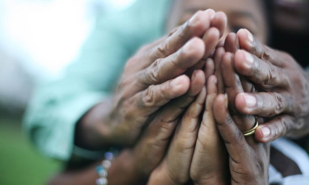 Three pairs of hands that are folded in prayer over eachother in agreement.