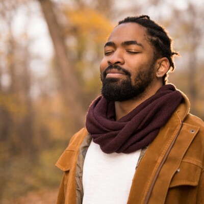 A man practicing silencing by standing in the forest with his eyes closed during the fall season.