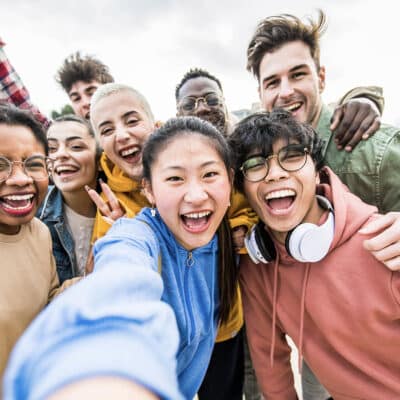 A diverse group of smiling young adults taking a selfie outdoors.