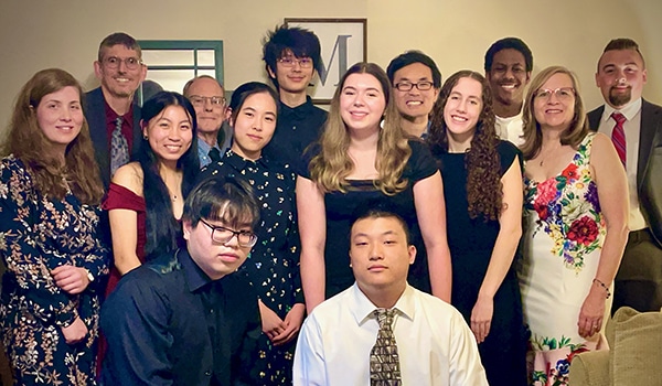 A group of young people dressed in formal attire posing together indoors.