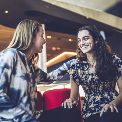 Sophia meeting with a friend in a coffee shop with a dark background and low lighting.