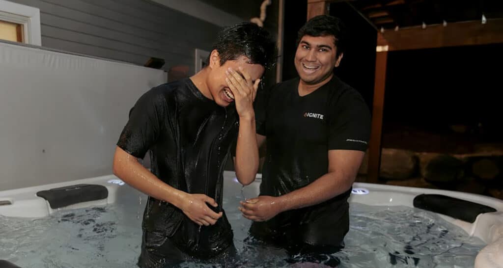 Two men standing in a small pool smiling after a baptism.