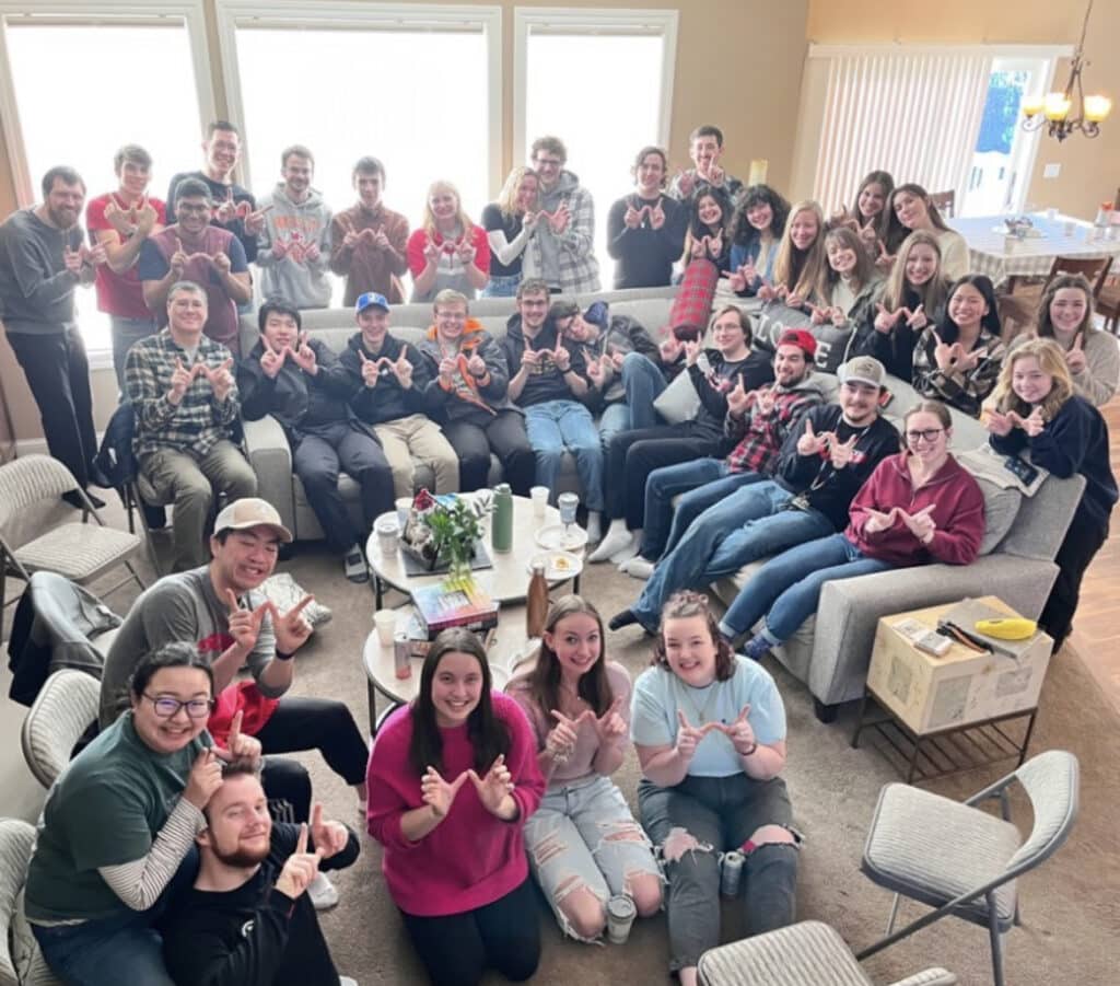 A group of young adults and college students in a living room scattered on the couch and floor.