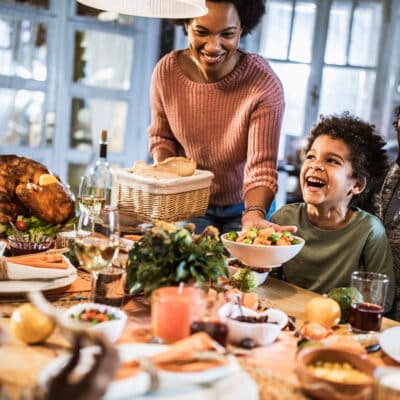 Family laughing and sharing a Thanksgiving meal together at the table.