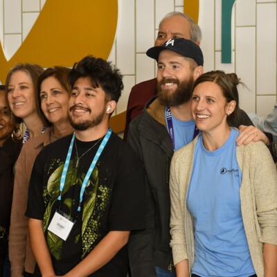 A group of Navigators staff stands together in front of The Navigators' logo.