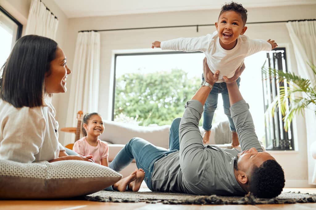 A family lays on the ground together while the father lifts up his son towards the ceiling.