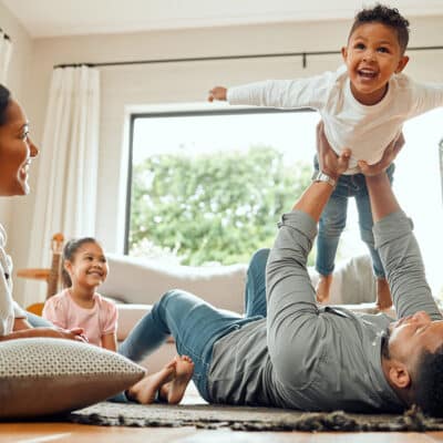 A family lays on the ground together while the father lifts up his son towards the ceiling.